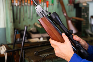 Closeup of gunsmith hands installing optical sight on smallbore single-barreled rifle in weapons workshop
