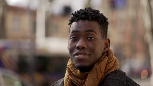 Portrait black African male smiling at camera wearing scarf outside in city