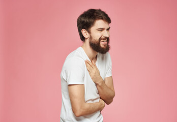 A man with a beard in a white T-shirt on a pink background gestures with his hands