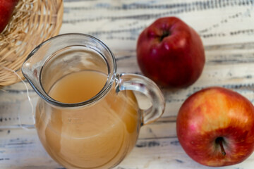 Red apples in a basket and apple juice in a jug on a wooden table