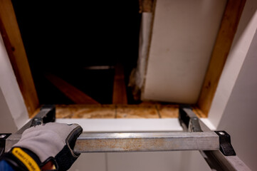 hand gripping the last rung on a ladder leading to an open attic