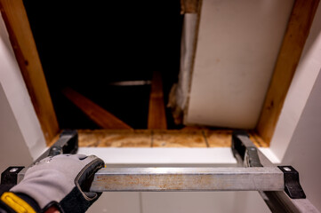 hand gripping the last rung on a ladder leading to an open attic