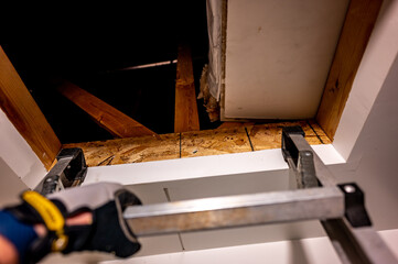 hand gripping the last rung on a ladder leading to an open attic