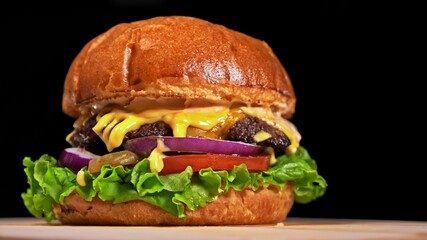Craft burger is cooking on black background. Consist: sauce, lettuce, tomato, red onion, pickle, cheese, bacon, air bun and marbled meat beef.