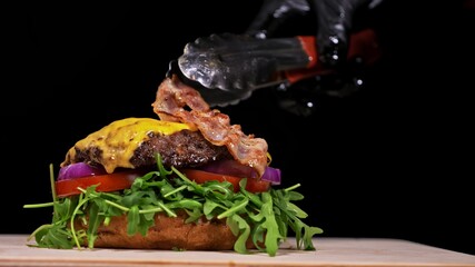 Craft burger is cooking on black background. Consist: sauce, arugula, tomato, onion, bacon, currant sauce, ricotta cheese, air bun and marble meat.