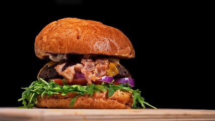 Craft burger is cooking on black background. Consist: sauce, arugula, tomato, onion, bacon, currant sauce, ricotta cheese, air bun and marble meat.