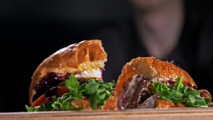 Cut craft burger is cooking on black background. Consist: sauce, lettuce, tomato, red onion,...
