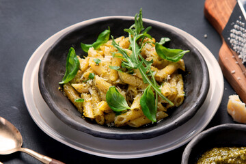 Pasta spaghetti with homemade pesto and fresh basil leaves on dark background. Italian cuisine concept.