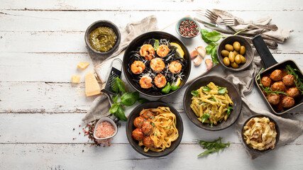 Assortment of Italian pasta with traditional snacks and sauces for dinner on white wooden background.