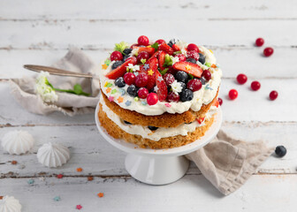 Delicious homemade cake with fresh berries and mascarpone cream on wooden background.