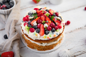 Delicious homemade cake with fresh berries and mascarpone cream on wooden background.