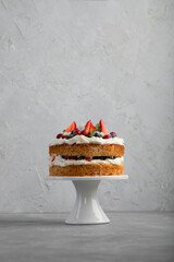 Delicious homemade cake with fresh berries and mascarpone cream on gray background.