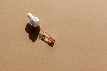 Dropper glass Bottle Cosmetic pipetteon brown background with copy space.Harsh sunlight.
