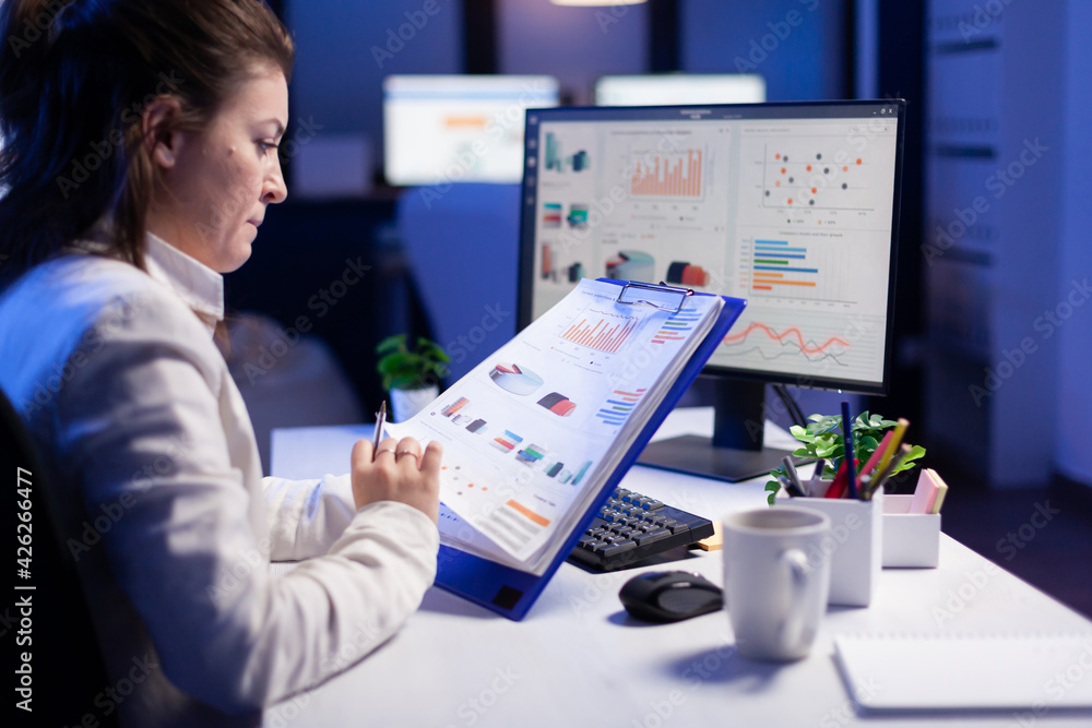 Poster freelancer woman comparing graphics from clipboard with grafics from computer at business office. ti