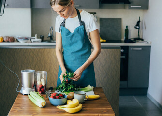 A female chef in a blue apron prepares a vegan fruit cocktail in her home kitchen. Healthy lifestyle and eating concept.