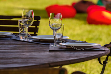 Beautifully laid tables with glasses and appliances in the cafe. Banquet service, catering. Empty wine glasses on a wooden table in an outdoor cafe.