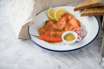 Asia Art Gravlax Graved Lachs, ein roh gebeizter Fisch mit Zitronengras und Chili auf Emaille Teller mit Hovmästarsås Senf Soße, Toast, Zwiebel Ringe, Dill, Zitrone und Leinen Tuch auf hell Marmor 