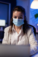 Close up of businesswoman with face mask checking emails late at night in new normal business...