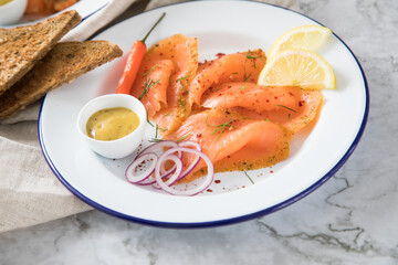 Asia Art Gravlax Graved Lachs, ein roh gebeizter Fisch mit Zitronengras und Chili auf Emaille Teller mit Hovmästarsås Senf Soße, Toast, Zwiebel Ringe, Dill, Zitrone und Leinen Tuch auf hell Marmor 