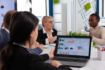 Young woman analysing charts on laptop in start up business meeting room. Multiethnic coworkers breefing team diverse people leadership. African employee listening senior manager.