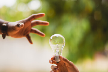 Businessman or electrical engineer In the hand holding the light bulb there is a natural background to experiment with solar energy. Electric power concept Solar energy Energy saving
