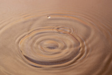 Fototapeta na wymiar Circles on the clear water and a drop hanging in the air. Under the water, you can see the sandy bottom