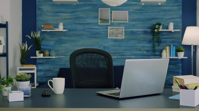 Empty workspace of freelancer worker with laptop computer on desk and cup of coffee. Interior of empty bright workspace with blue furniture and walls, beautiful decorated, cozy apartment