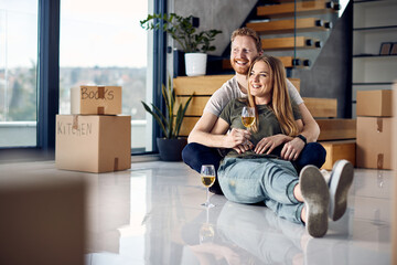 Happy couple drinking wine and relaxing on the floor at their new apartment.