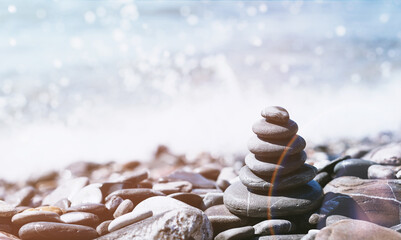Stone pebble tower balancing on the beach with sparkling sea waters splash bokeh. Copy space. Balance and mindfulness. Summer travel and vacation. rainbow reflection
