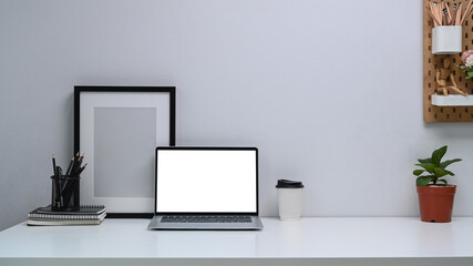 Home office desk with computer laptop, pencil holder, house plant, black empty photo frame and coffee cup.