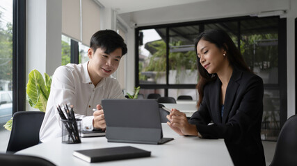Two happy businesswoman using computer tablet and discussing business idea in modern office.