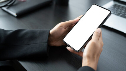 Mock up image of businesswoman holding mobile phone with empty screen over black wooden table.