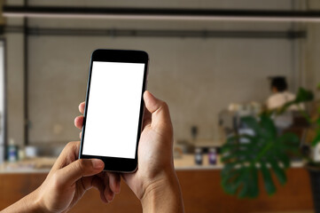 Hand holding white mobile phone with blank white screen in cafe.