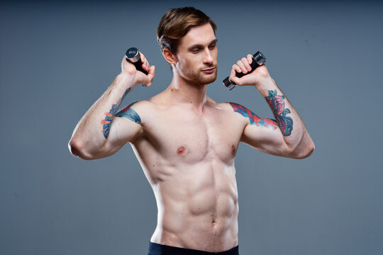sexy athletic men with dumbbells on gray background and biceps press tattoos
