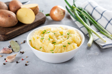 Mashed potatoes in a bowl on a white wooden table with fresh herbs on a gray background