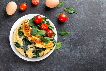 Omelet with spinach leaves. Omelette on plate, scrambled eggs on a dark slate or concrete background. Top view. Copy space.