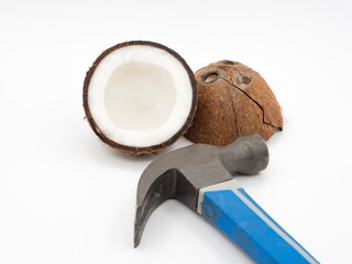 Two coconut halves with the pulp broken and split with cracks on a white background next to the hammer. The concept of eating exotic fruits.
