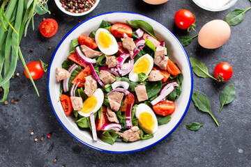 Salad from the liver of codfish, eggs, spinach and tomato on a plate on a dark slate, stone or concrete background. Top view. Copy space.