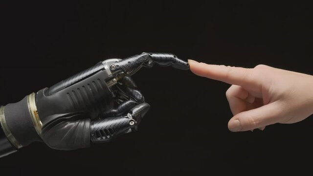 Humanoid robot arm and human hand reach out to each other and touch with fingers on black background. Interaction of artificial intelligence and human mind.