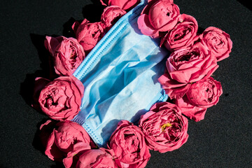 New normal mock up, pink roses or peonies with blue medical protective face mask. Creative...