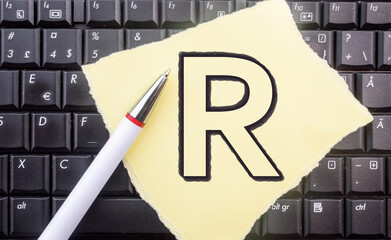 R programming language. Letter R on paper and laptop