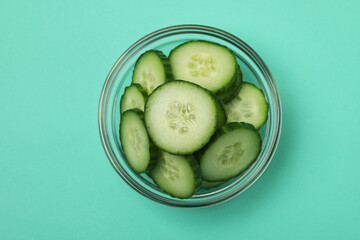 Bowl with ripe cucumber slices on mint background