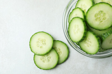 Bowl with cucumber slices on white textured background