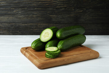 Board with ripe cucumbers on white wooden table