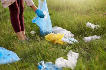 Faceless female volunteer wearing leggins and gloves picking up litter in meadow, using blue...