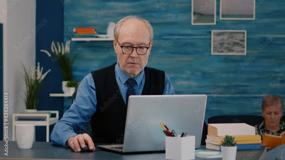 Poster senior businessman reading reports sitting in front of laptop working from home drinking coffee. ret