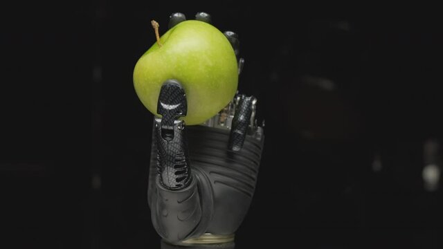 Humanoid robot hand holding green apple on black background closeup. Concept of new technologies.
