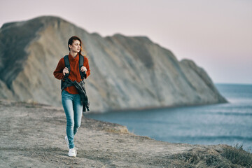  woman in sweater jeans and sneakers on the seashore and mountains in the background 