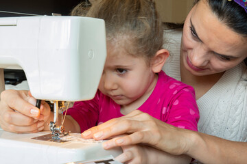 little girl is learning from her mother to use a sewing machine. selective Focus arm