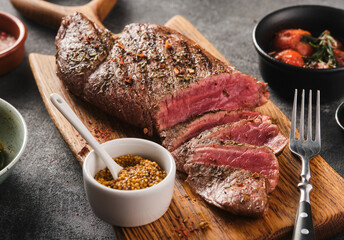 Sliced BBQ steak medium rare with salad and garlic on the grey background. Hip steak on wooden board